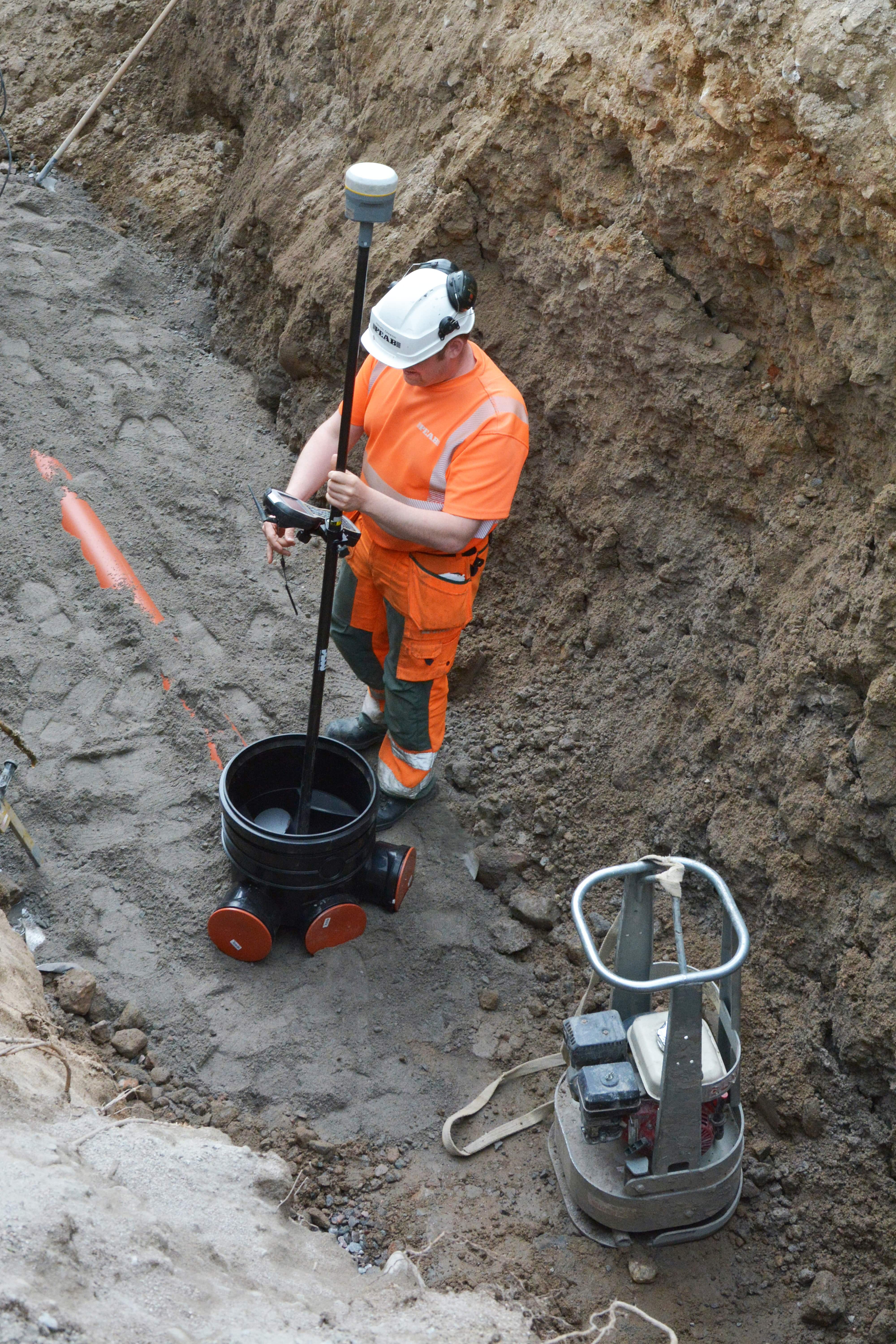 A surveying engineer is standing in a conduit trench, surveying pipes with RTK.